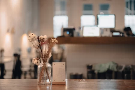 closeup-shot-cafe-wooden-table-with-jar-decorative-flowers-against-blurred-background